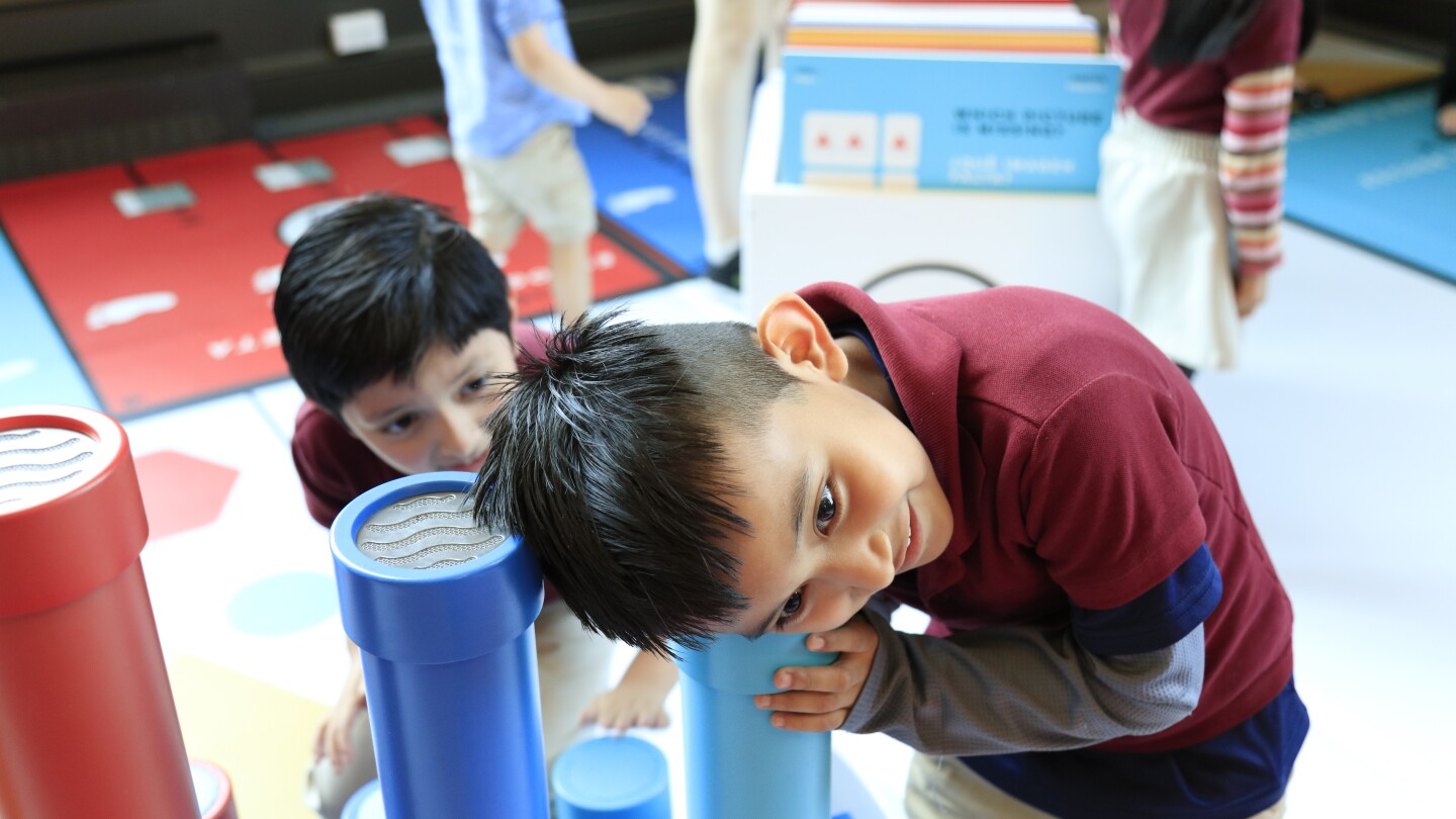 A small boy smiles as he places his ear over a colorful tube and listens.