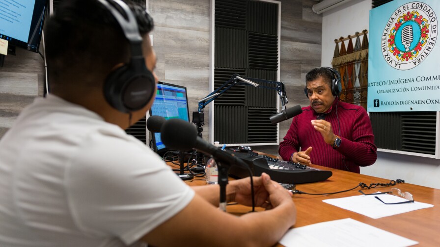 Francisco Didier Ulloa and Bernardino Almazán sit across from each other in a radio studio decked out with sound dampening on the walls and microphones on a table.
