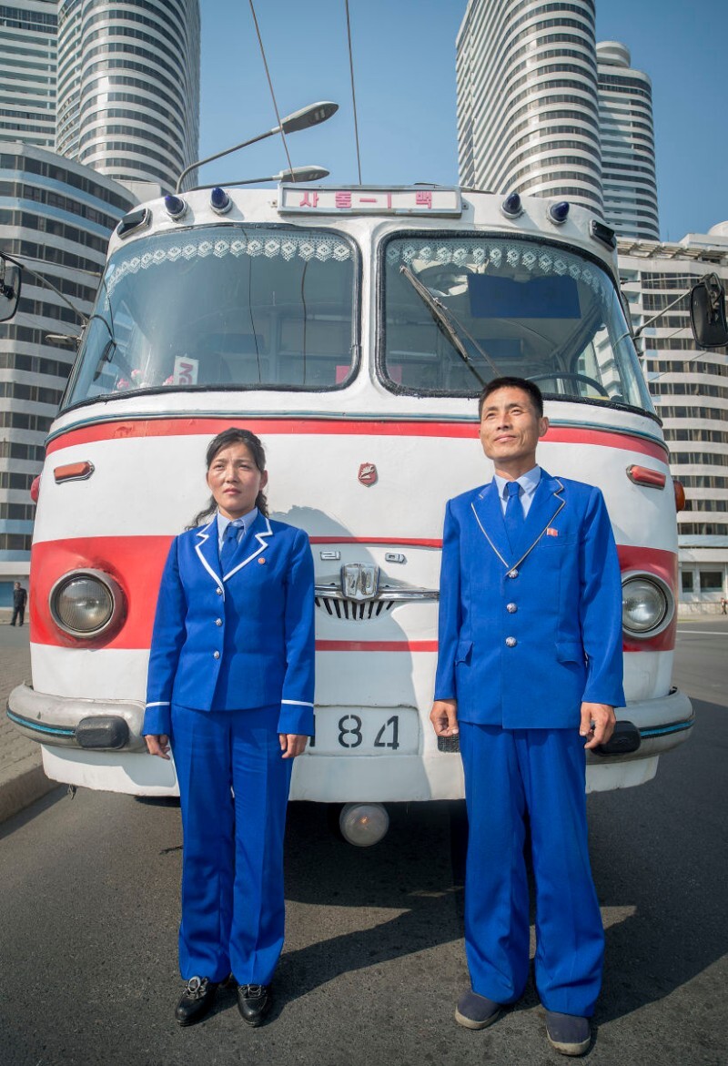 A bus driver and ticket taker stand in front of the historic bus that Kim Il Sung rode on. North Korea | Mark Edward Harris