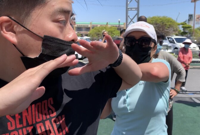 An older Vietnamese American woman practices self-defense moves on a volunteer.