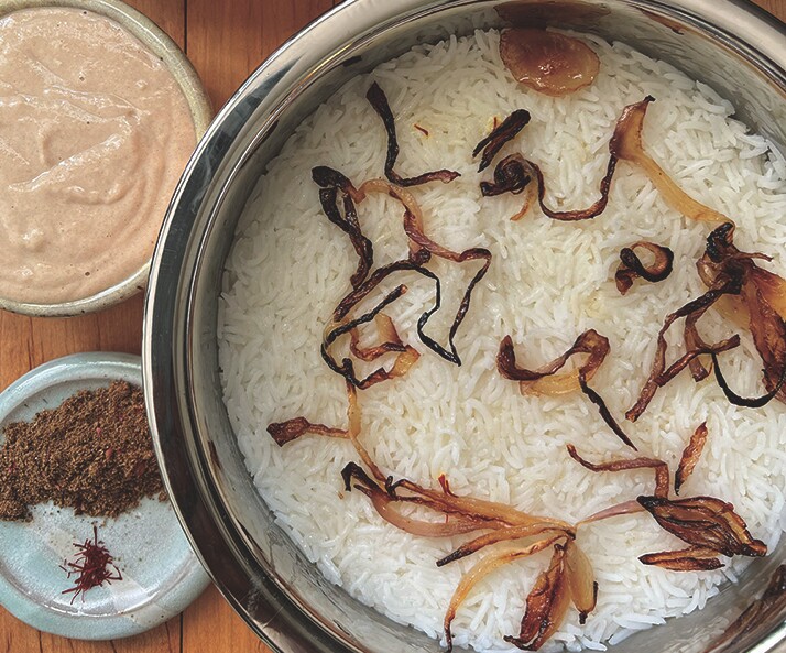 A small, brown pot of biryani. Next to it is a small bowl with brown spices. 