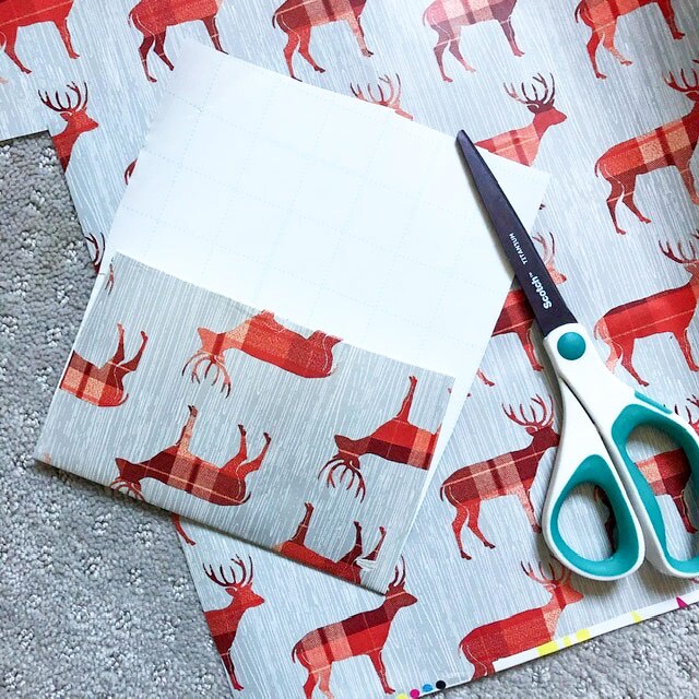 A folded piece of wrapping paper with red reindeer with some scissors next to it.