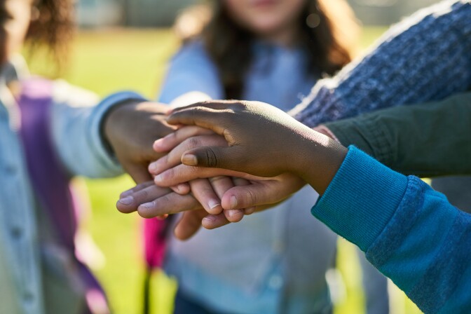Shot of a group of unrecognizable elementary school kids joining their hands together in a huddle outside