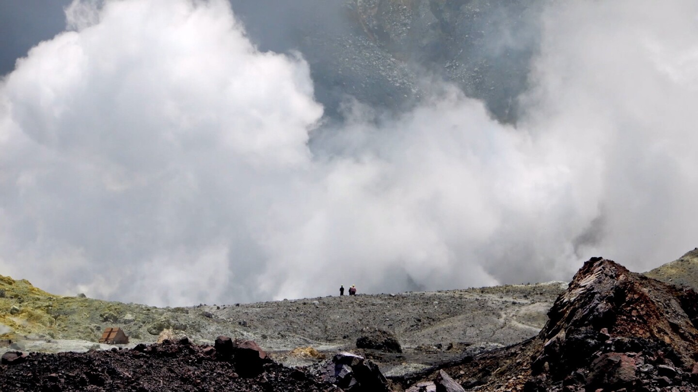 People at a distance stand atop a hill overlooking a massive cloud of smoke.