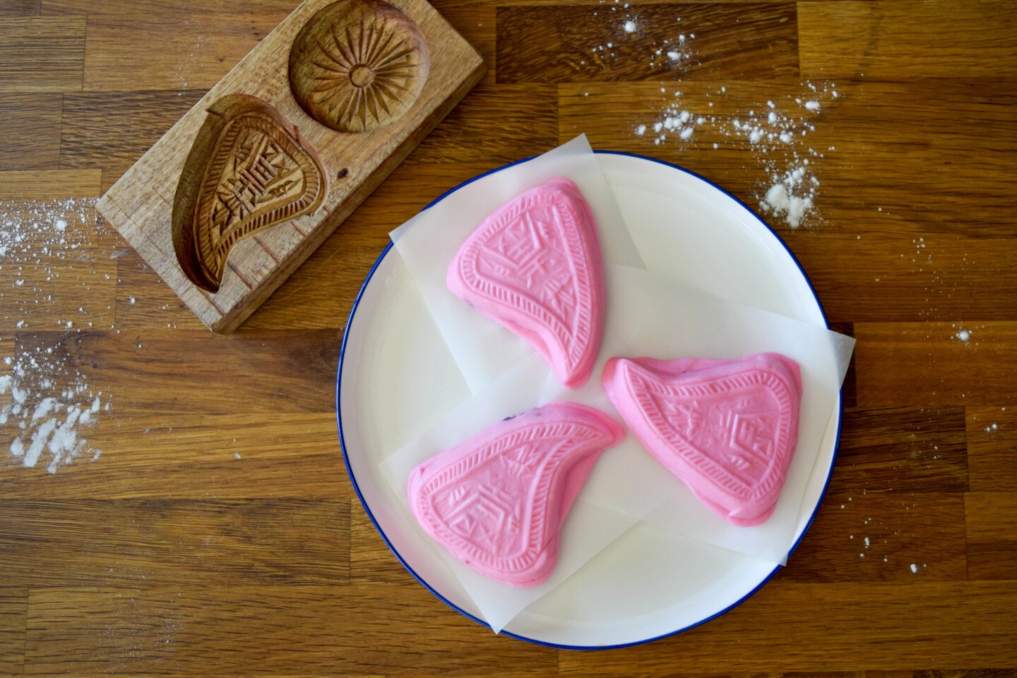 Three pieces of ang to gue, a traditional savory pink peach-shaped rice dough, sit on a plate.
