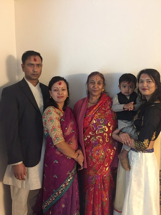 Three women, one holding a small child, in saris stand next to a man.