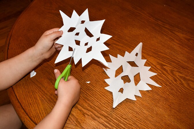 A child's hands cut out paper snowflakes.