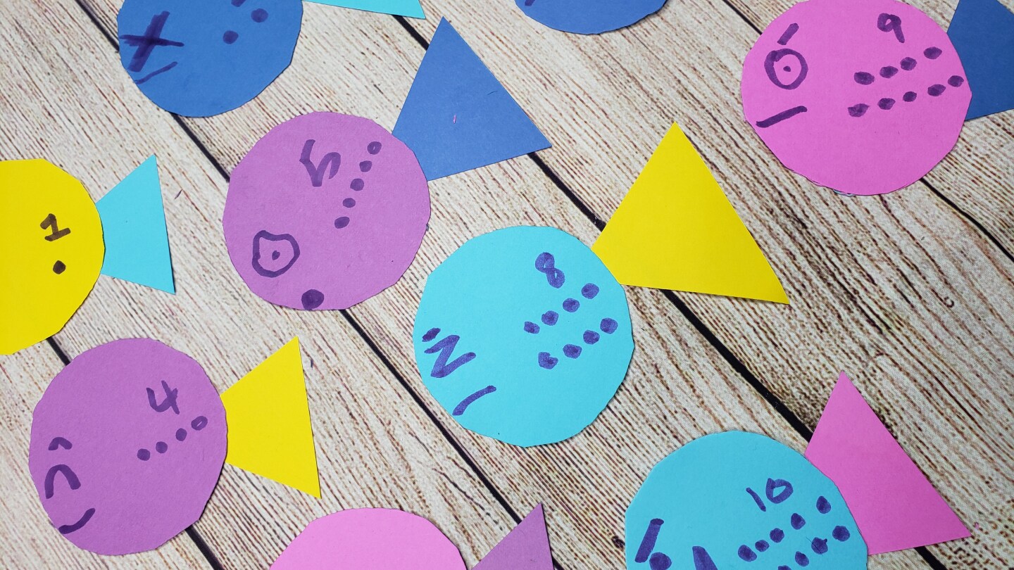 Colorful cutouts shaped like fish, each labelled with a number from one to 10, are lined up on a wooden table.