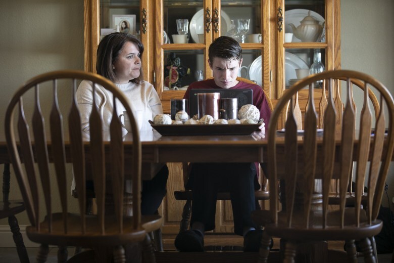 Daniel and his mother, Linda, sit at their dining room table. Daniel's brow is furrowed as he looks down at a black laptop. His mother sits next to him.