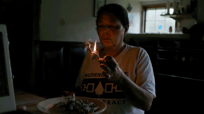 A woman gently blows on a flame in a low lit room. | From "Independent Lens: Conscience Point"
