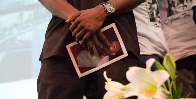 A friend of Josiah Lawson at his memorial, holding a photo of David Josiah Lawson in his hands. | Still from "Who Killed Josiah?" | Courtesy Mark McKenna