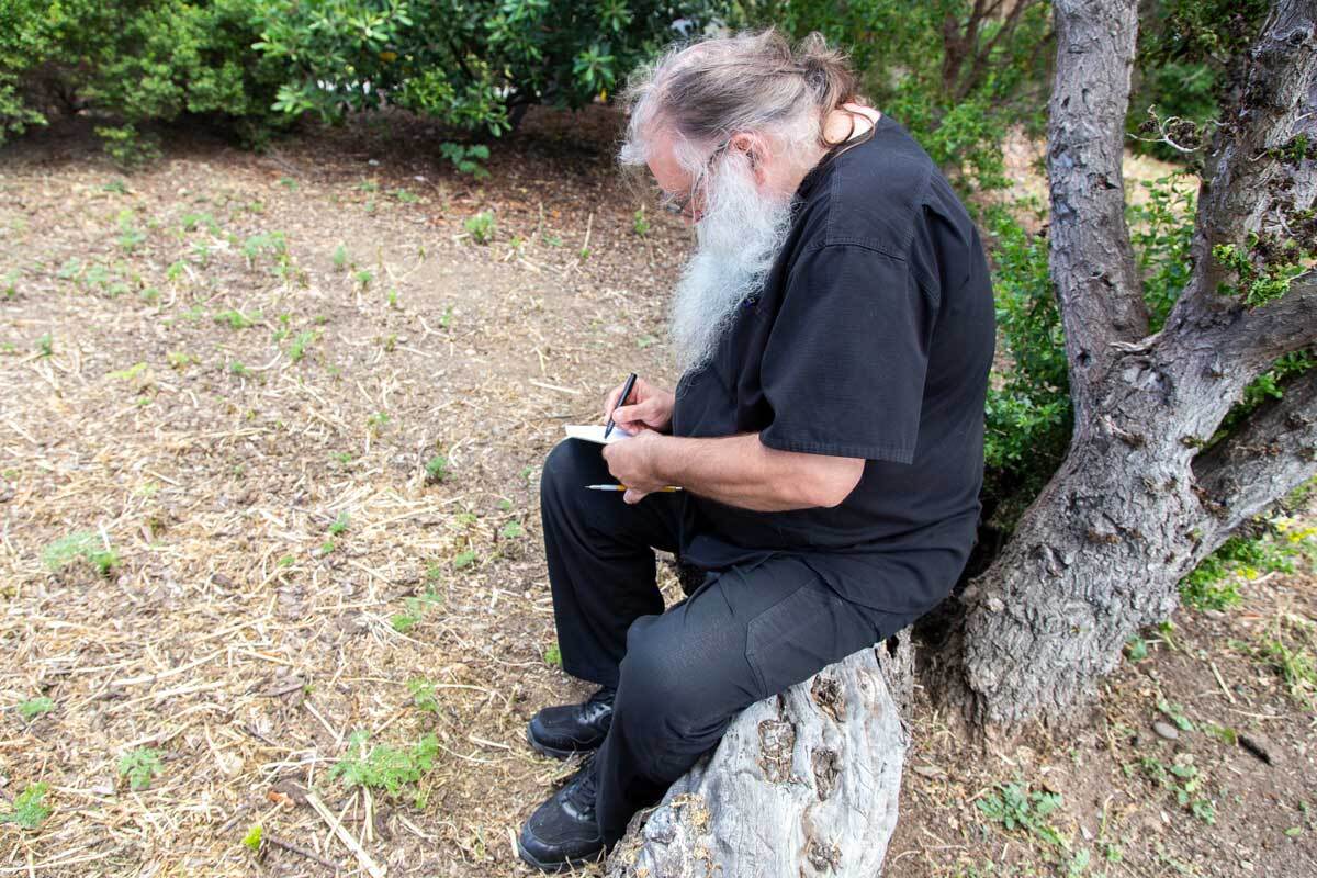 Thomas Zummer drawing while sitting on a log at San Clemente Border Station for "Three Border Ecologies" | Lena Martinez Miller