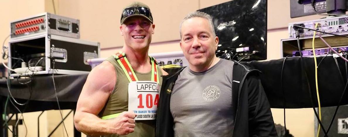 Sheriff Alex Villanueva in a shirt with the Fort Apache logo poses with a competitor at the annual Baker to Vegas event in March 2019 Cropped