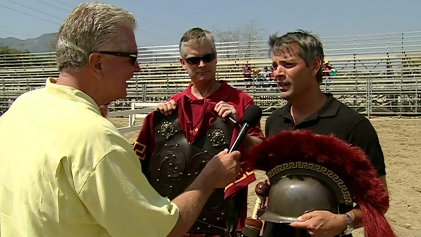 Huell points his mic at a man holding a Trojan helmet.