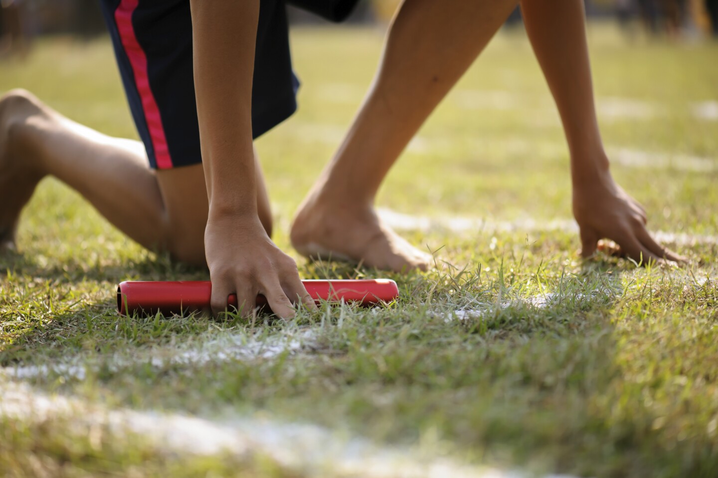 The athlete holding the relay race wood baton, is kneeling down on the track, preparing to start the first leg of a relay race. family math relay activity olympics