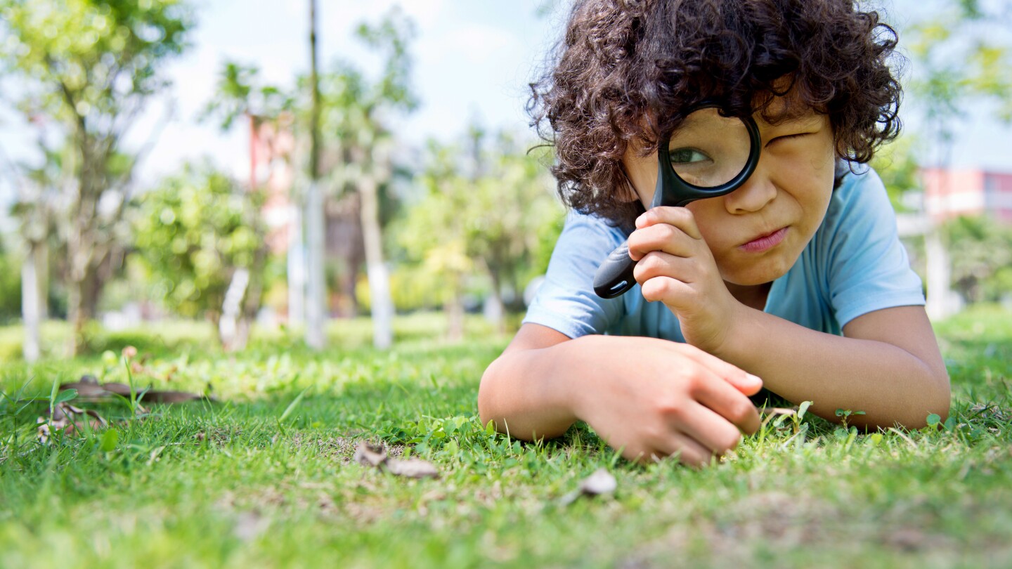 Little boy with magnifying glass in park outside community science citizen science neighborhood sicence