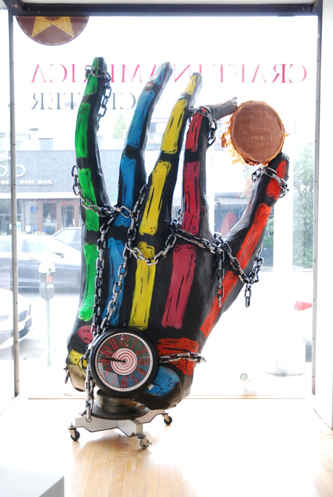 A hand-shaped piñata holds a coin up to a window.