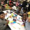 Children and their parents from Compton’s McKinley K-8 School of Integrated Arts smile at the camera while doing arts and crafts activities.