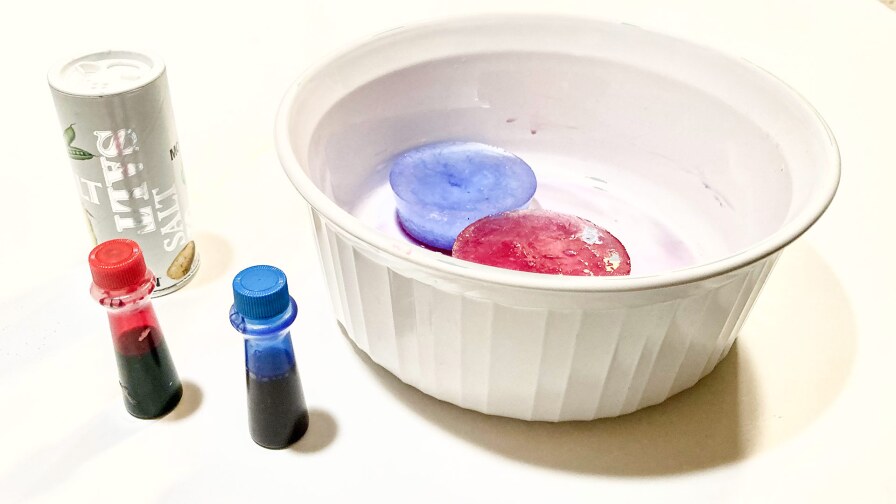 Two colorful ice cubes painted with food coloring (one blue and one red) sit in a bowl.