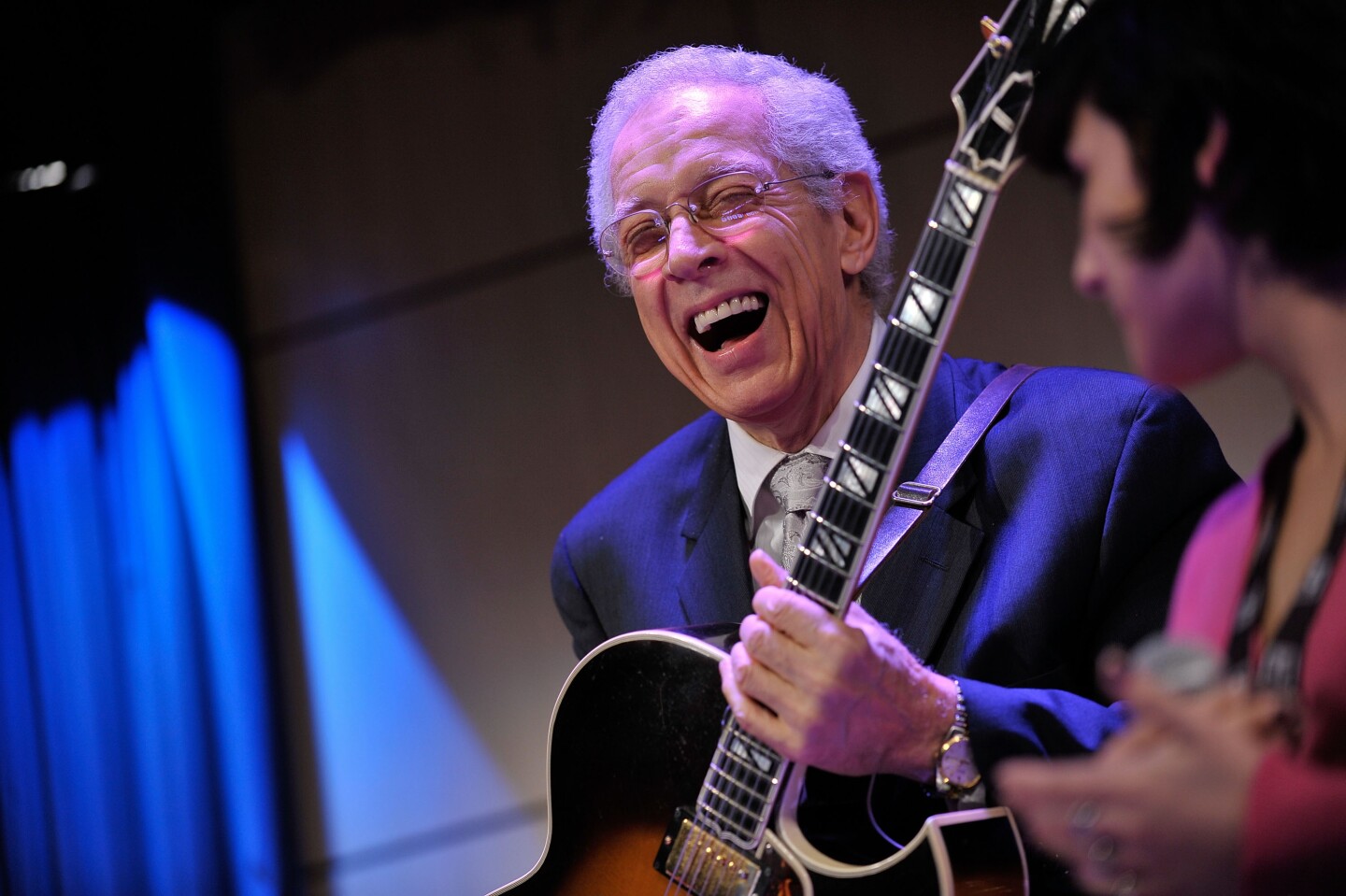 Kenny Burrell is an older man holding a guitar smiling wholeheartedly