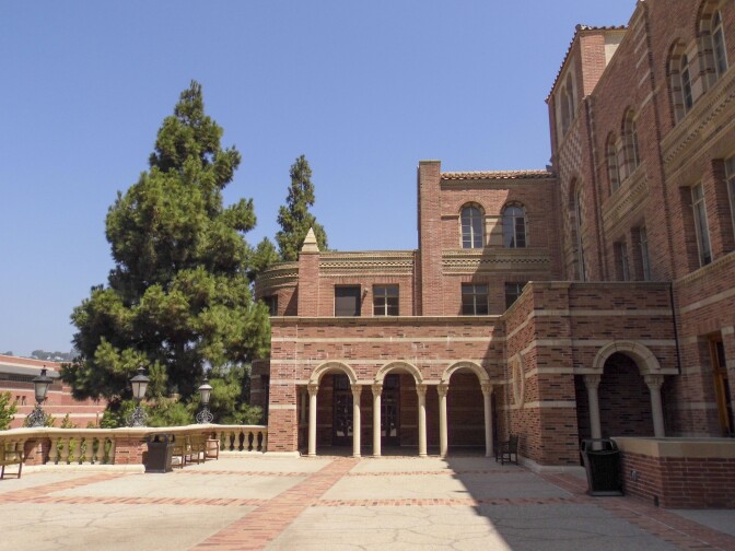 An exterior photo of Royce Hall on the UCLA campus. The photo captures the building's side. The building is predominantly composed of red bricks.