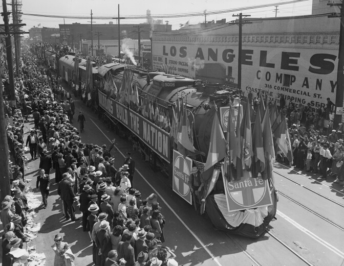 A train carrying many flags rolls over the rails with a banner announcing, "Railroads build a nation" During a parade to celebrate the opening of LA Union Station.