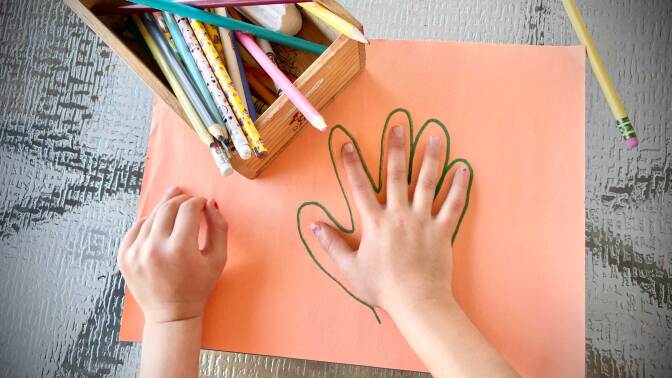 Chld tracing hand on orange construction paper.