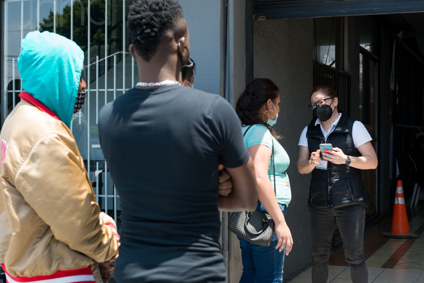 Two people wait in line behind a woman speaking to a volunteer in a black vest.