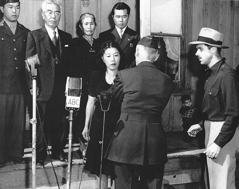 A black and white photo of a woman being pinned with an honorable pin. In front of her are various microphones. Behind her are her family members.