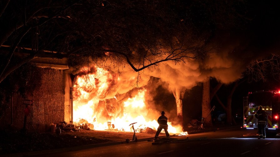 Sacramento firefighters stand just beyond a homeless encampment fire.