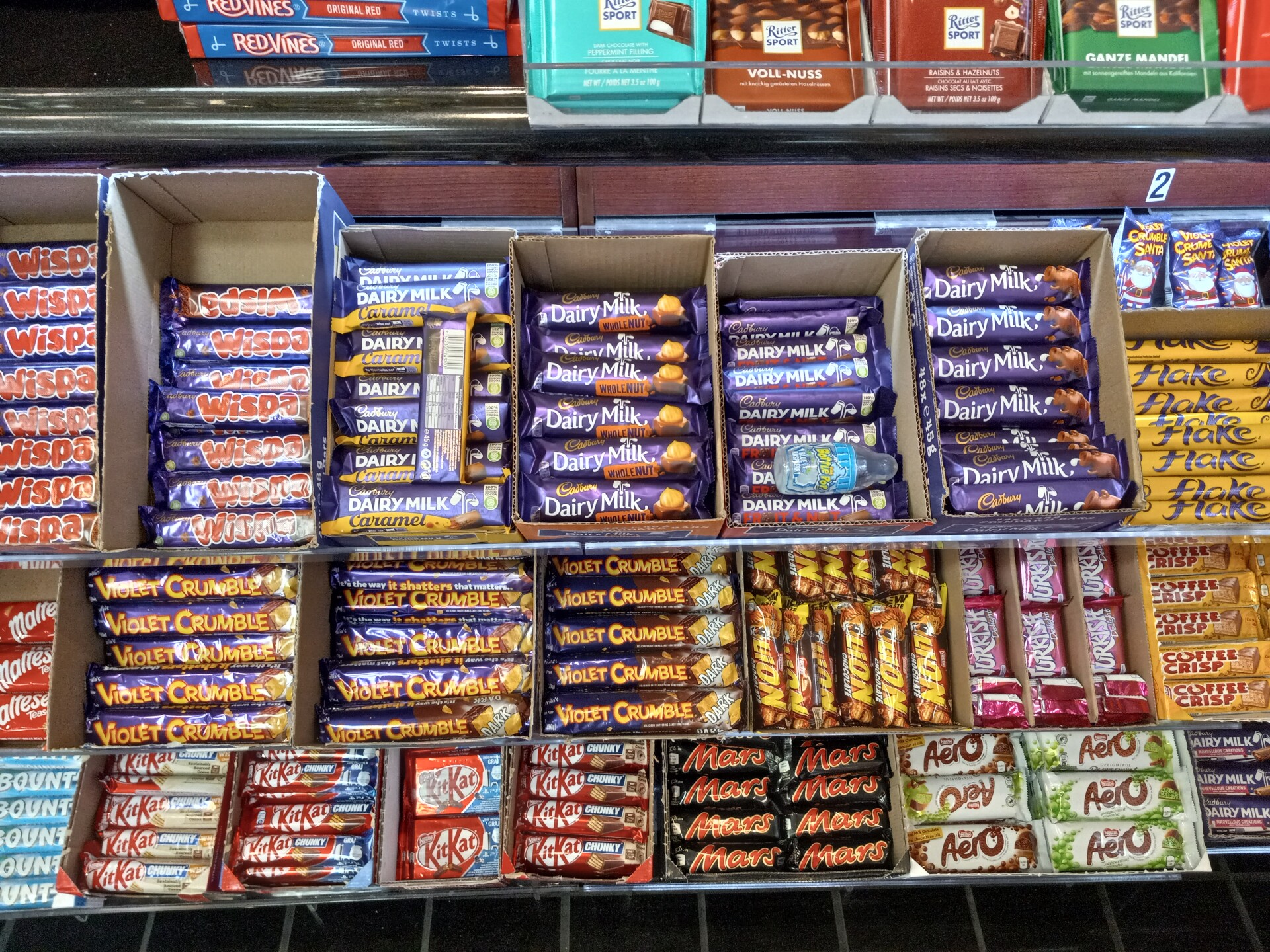 Boxes of chocolate and candy are arranged together in a rack at a gas station convenience store.