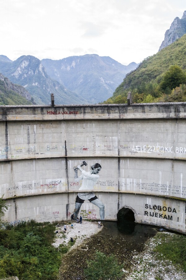 a large damn with graffiti of a woman with a hammer on it, mountains in the background