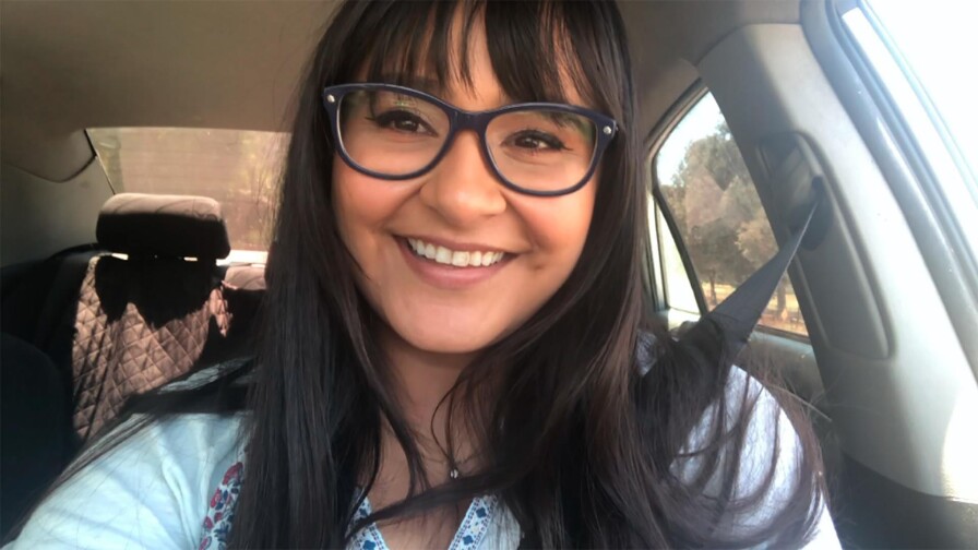 A person with glasses is sitting by the wheel of a vehicle.