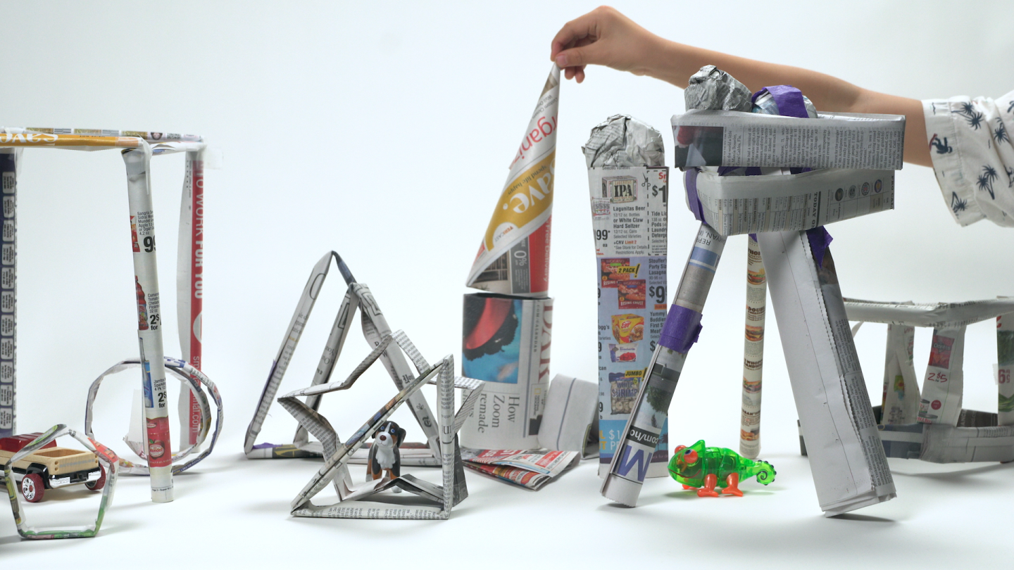 Several shapes and structures made out of newspaper are peppered with small toys.