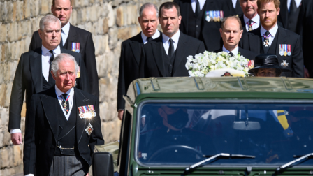 A crowd of men including Prince Charles, Prince Edward and Prince Harry walk behind a Land Rover truck carrying Prince Philip's casket.