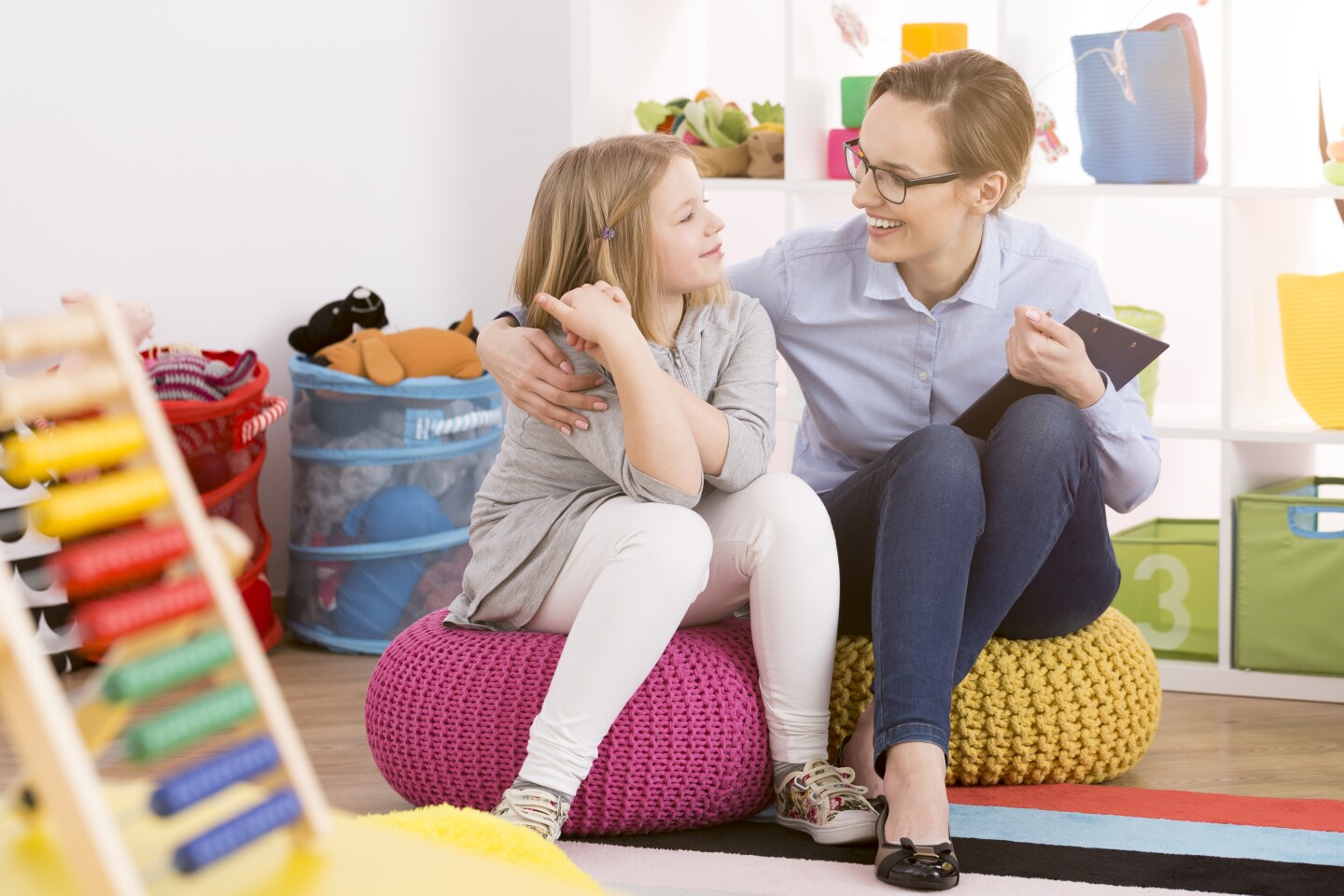 A woman sits next to a child in a colorful educational playroom.