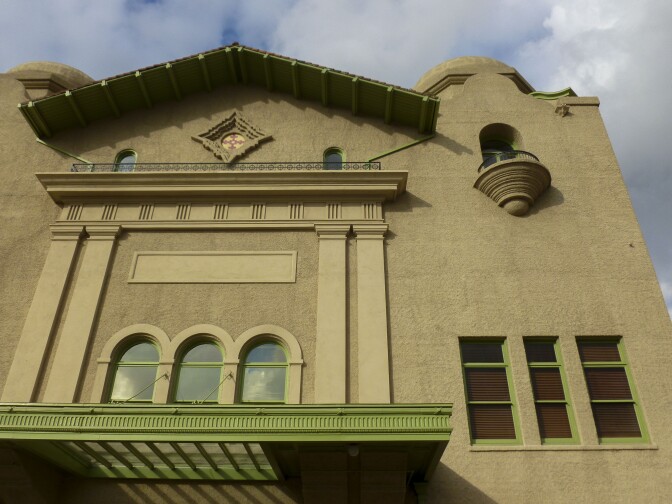 The exterior of the Santa Fe Depot in San Bernardino features a beige concrete face with arched windows and domes that top the building. A vibrant, lime green trim lines each windows and the underside of the roof.