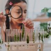 A little girl looks at test tubes through a magnifying glass. iStock