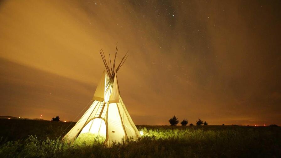 A Native American teepee is lit up against a vast, empty field. | "Native America: New World Rising"