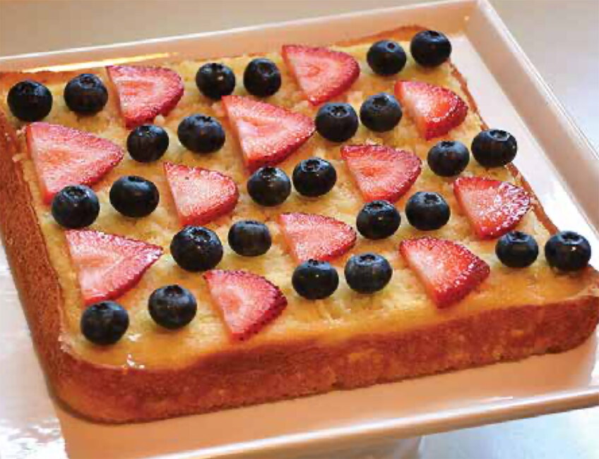 A yellow cake topped with neatly arranged strawberries and blueberries