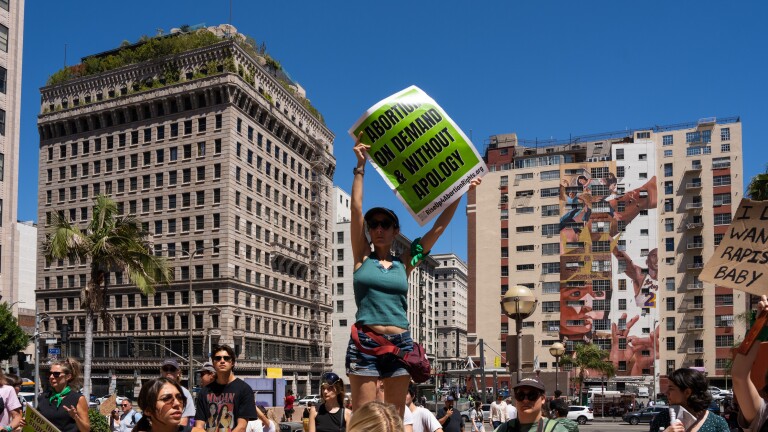 A woman stands above a crowd in Downtown L.A. holding a sign that reads "Abortion on Demand & Without Apology"