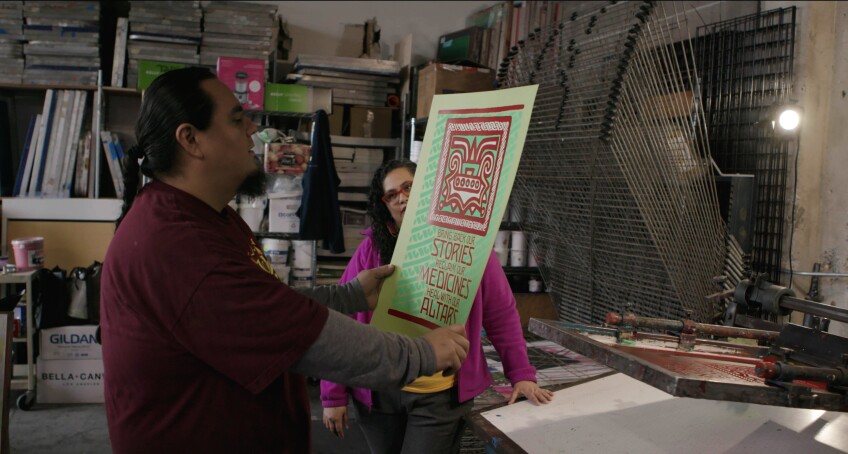 A man in a long-sleeve shirt holds up a graphic design poster in a studio.