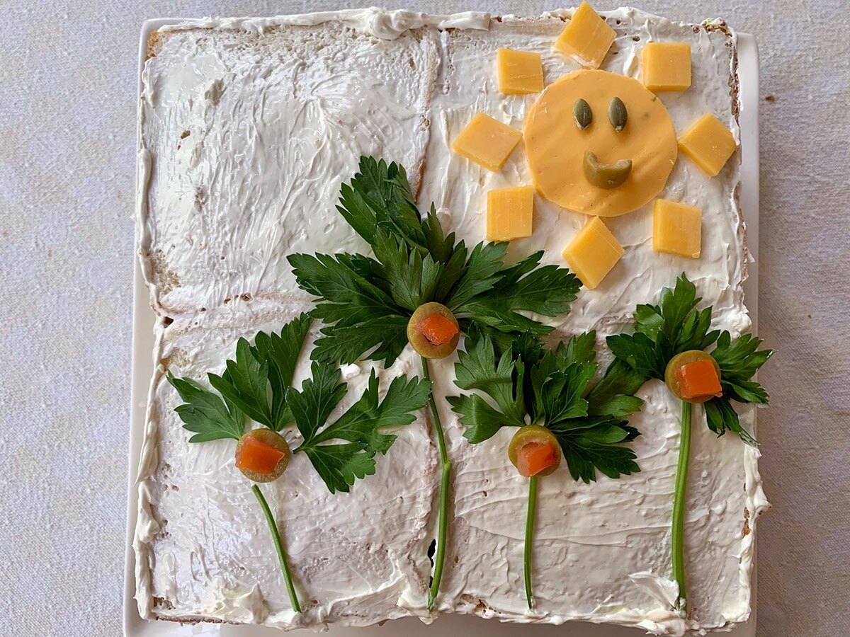 Vista superior de un sandwichón decorado con flores de perejil y un sol sonriente de queso