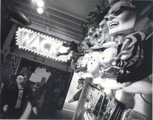 A neon sign that reads "WACKO" and walls covered with face masks adorn the interior of the store.