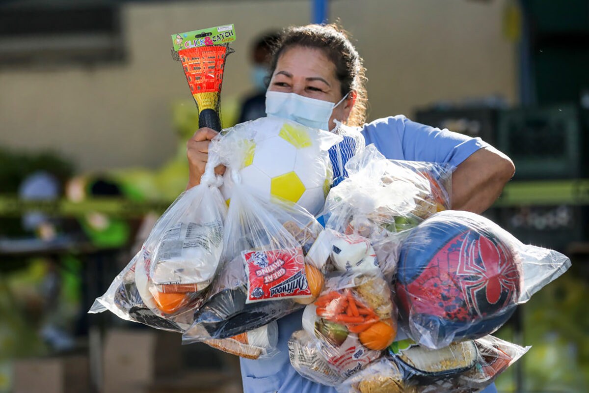 Beatrice Lopez walks out with sports items and meal bags distributed by LA84 Foundation and LAUSD at Grab and Go center at Thomas Alva Edison School.
