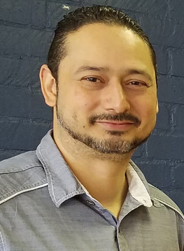 Carlos Aguilar smiles while wearing a grey button-down shirt.