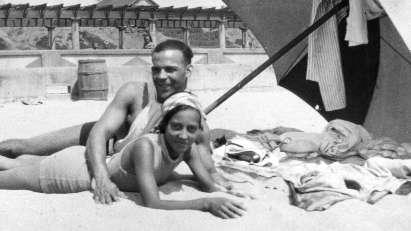 A minority couple laying on the beach together under an umbrella