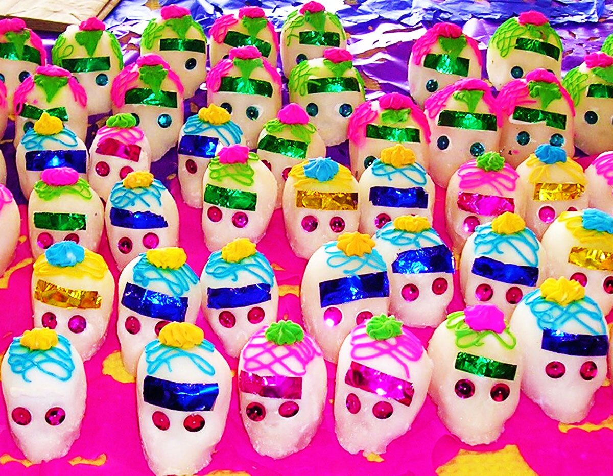 A pink table is covered in vividly decorated tiny sugar skulls.