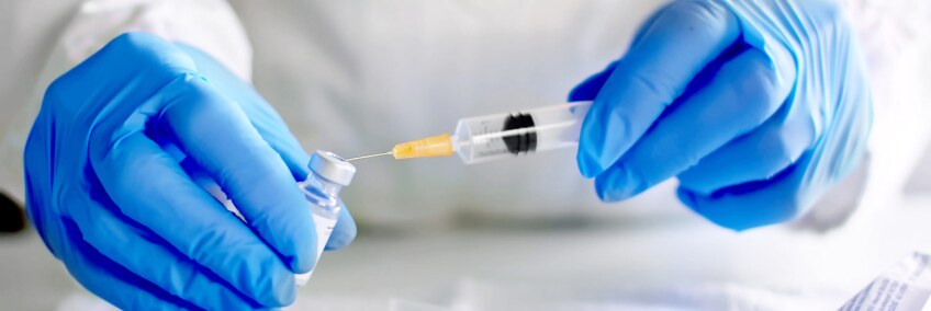 A medical worker wearing gloves fills up a needle with a vaccine. | iStock via Getty Images