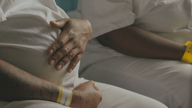 A pregnant woman in prison uniform places a hand over her belly. | From "America ReFramed: Tutwiler"